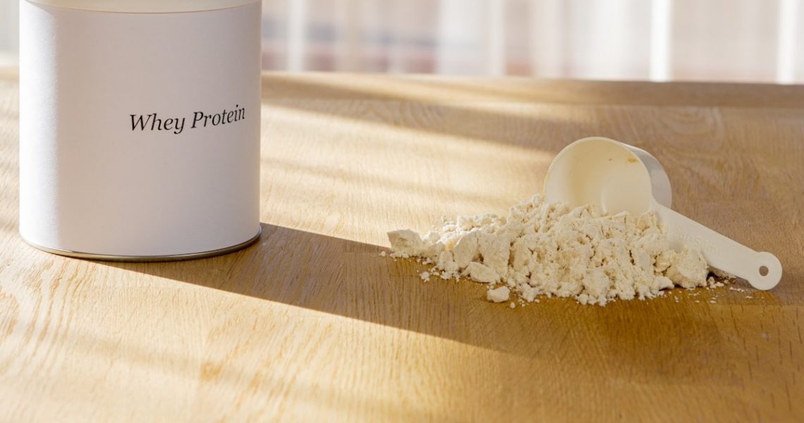 Protein powder container and measuring scoop on wooden surface, gym supplement